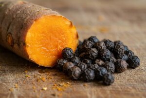 aspirin plant medicine,microbiome A macro shot of turmeric root sliced open, showing its bright orange interior, placed next to a small pile of black peppercorns. This highlights the concept of natural synergy.