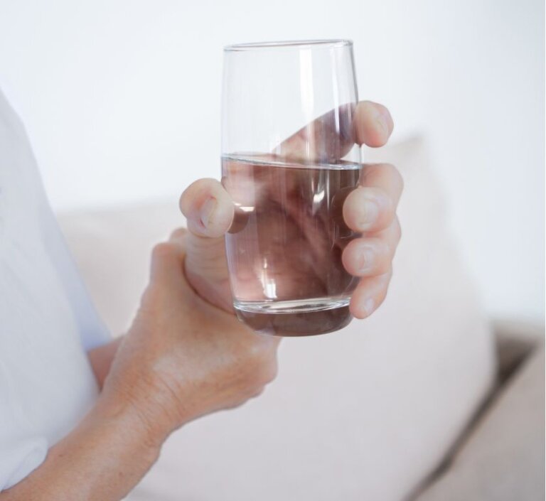 Parkinson's patient holding glass with both hands due to tremors